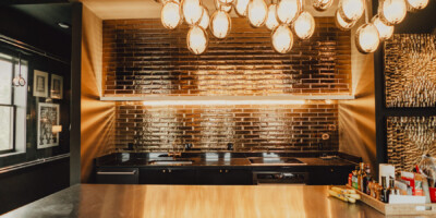 Modern kitchen with shiny metallic backsplash, overhead orb lighting, and stainless steel island with various items on the counter.