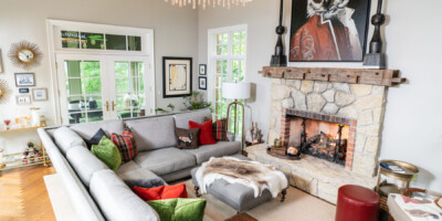 A modern living room with a gray sectional sofa, stone fireplace, and a large owl painting above the mantel.